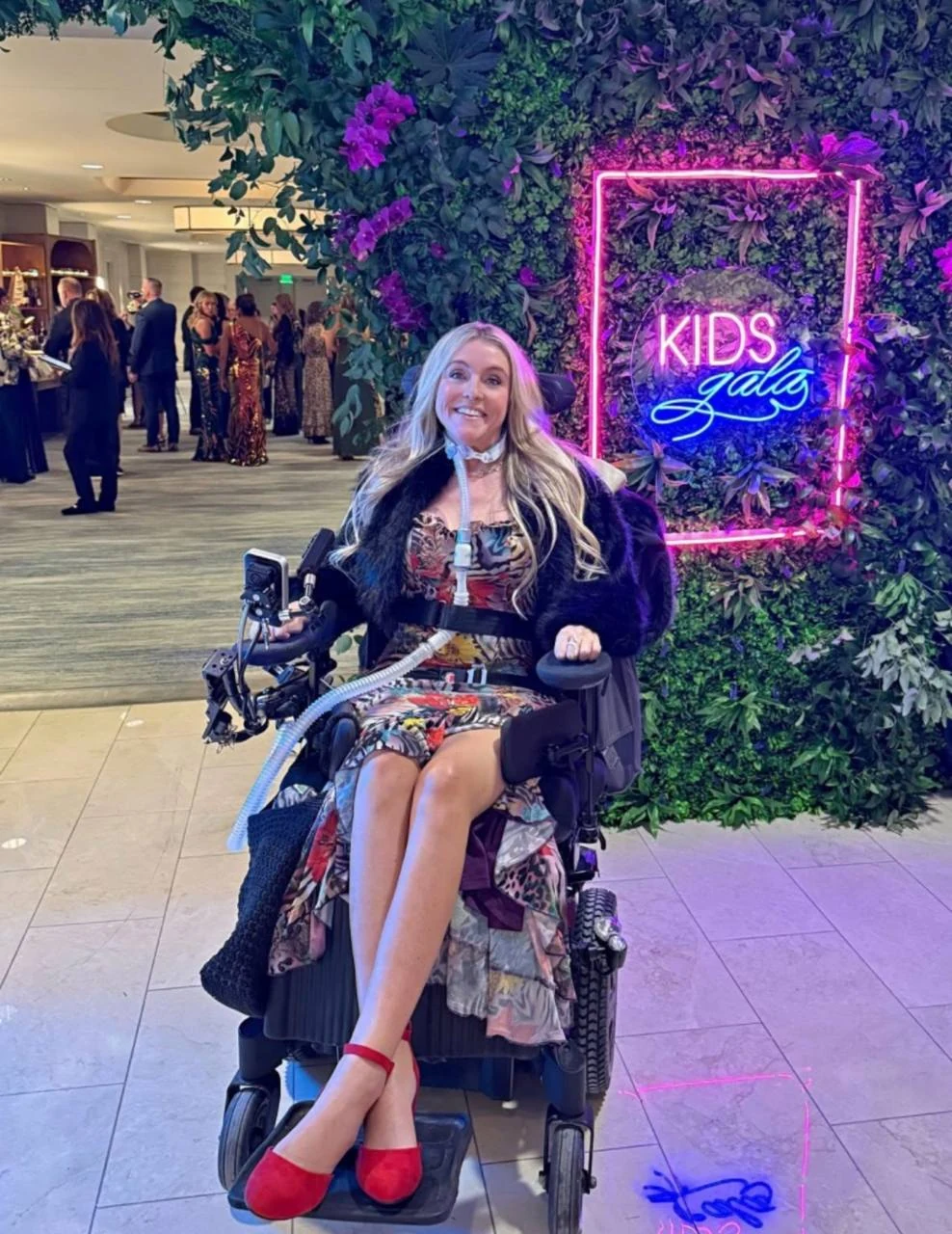 Laura Michelle at a gala in front of a neon sign and flower wall.