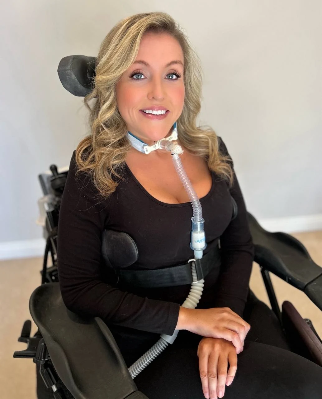 Laura Michelle smiling in a black outfit while seated in her wheelchair.